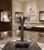 A pair of silver finish, American diamond jumbo jhumka earrings displayed on a stand against a black background.