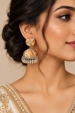 A close-up photograph of a pair of handcrafted Indian jhumka earrings displayed on a black t-shaped stand. Each earring features a round stud and a dome-shaped bell, both made of metal and featuring a detailed, multi-colored Kalamkari-style art print with floral and paisley motifs. The bottom of each dome is adorned with a fringe of small, hanging silver-colored metal beads. The background is a plain white surface, with a black textured display stand. The lighting is even and clear.
