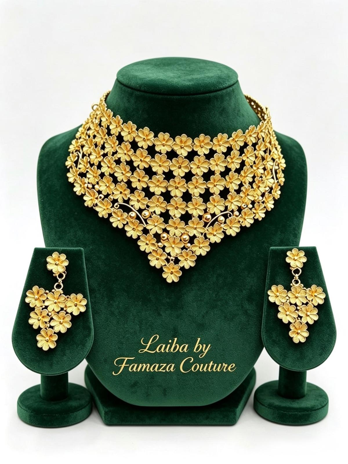 A luxury gold-plated Laiba floral statement collar necklace and matching chandelier earrings displayed on a green velvet stand, by Famaza Couture.