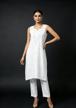 A model wearing the white handcrafted sleeveless Chanderi silk Chikankari co-ord set, posing against a solid dark background.