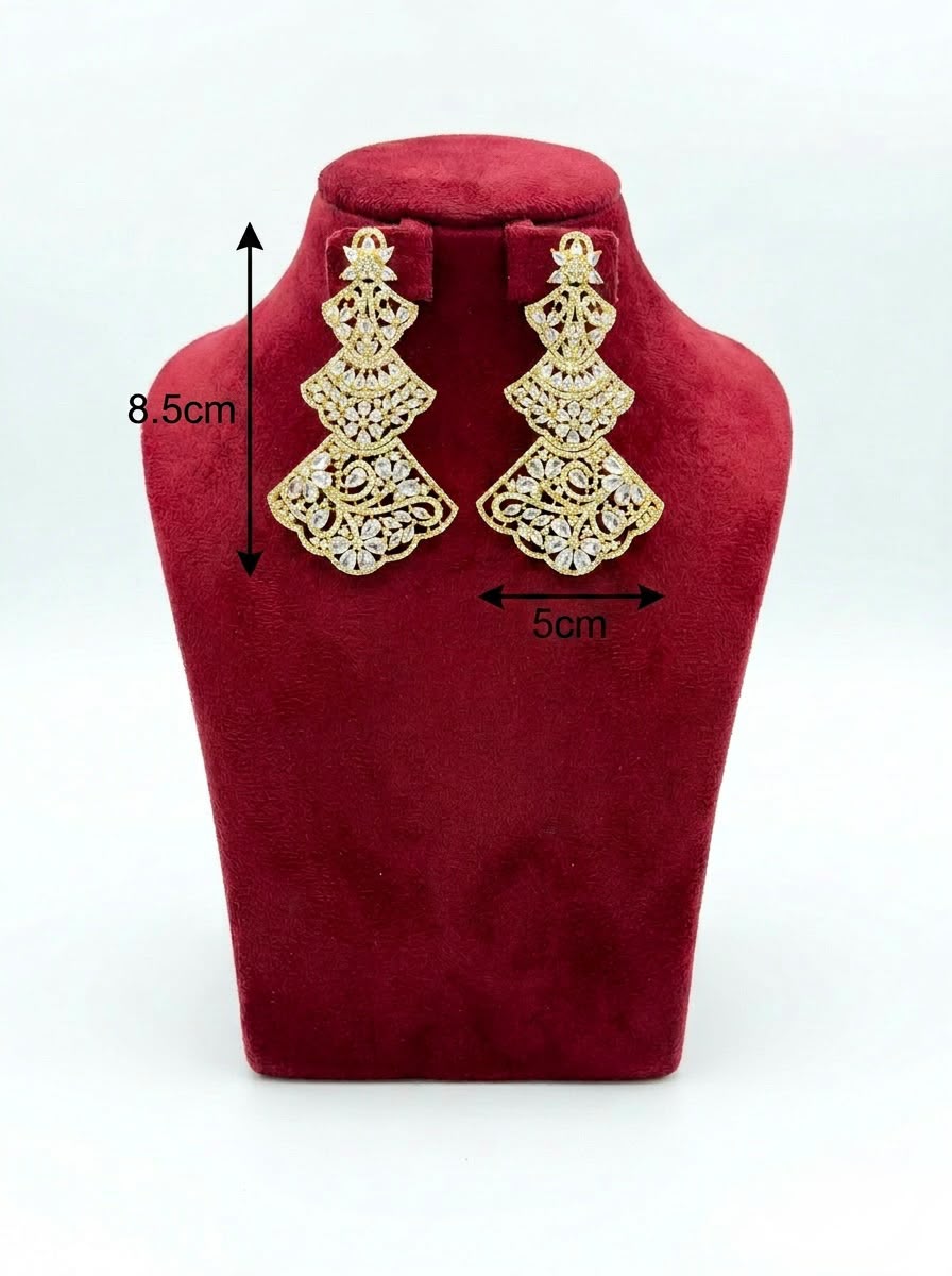 Pair of three-tiered gold-tone statement chandelier earrings featuring intricate filigree metalwork and sparkling clear cubic zirconia crystals, displayed on a red velvet jewelry bust.