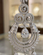 A close-up view of an intricate, silver-toned chandelier earring featuring a central pear-cut crystal, surrounded by detailed filigree metalwork and rows of sparkling baguette and pavé-set stones."