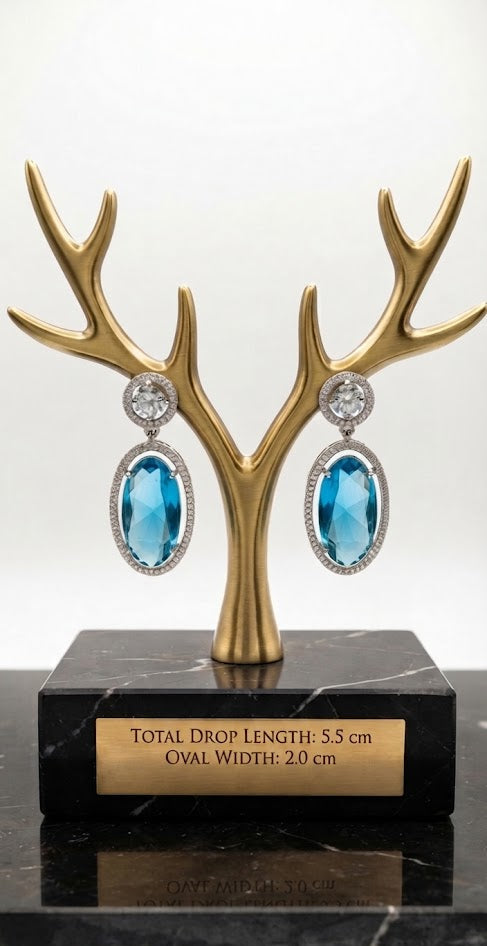 Luxury blue oval cut drop earrings featuring diamond halo accents, displayed on a gold antler stand with dimensions 5.5 cm long and 2 cm wide on an engraved plaque.