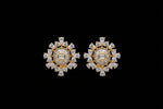 Gold-toned statement earrings with clear round and marquise-cut stones, shown worn on a hand against a dark textured background.