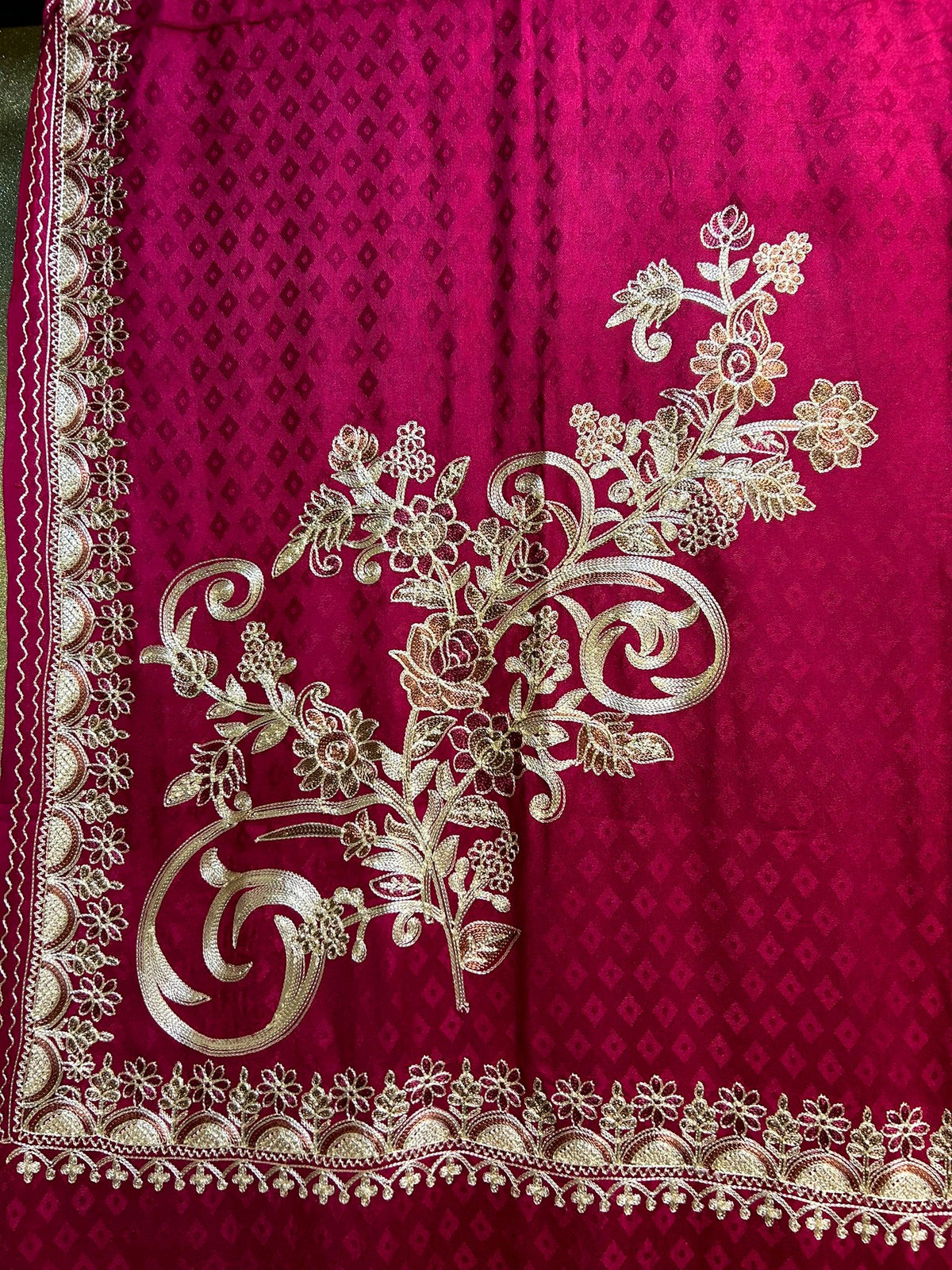 Maroon Kashmiri Aari embroidered marina scarf with tassels hanging at the ends, displayed on a wooden hanger with greenery in the background.