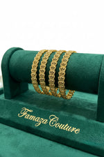 A set of four micro-gold plated copper bangles featuring an intricate fan-shaped lattice pattern, displayed on a luxury green velvet Famaza Couture jewelry stand."