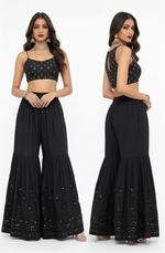 A dual-view studio photograph showcasing the front and back of a model wearing a premium black cotton flared gharara, detailed with intricate handcrafted Kaamdani embroidery along the hem, set against a crisp white background.