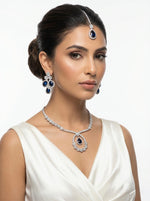 Model is wearing The American diamonds bridal jewellery set including necklace, earrings and maang tikka with purple colour central cubic zirconia stones.