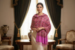 Model is wearing a pink base colour floral multi-colour embroidered shawl in an elegant room with curtains and furniture.