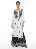Model is wearing a white outfit with black floral hand embroidery on a white background with black trousers .