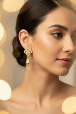 Model wearing golden brass earrings with a shimmering pave-set starburst stud and a dainty, crystal-encrusted bell-shaped drop hanging from a delicate link.