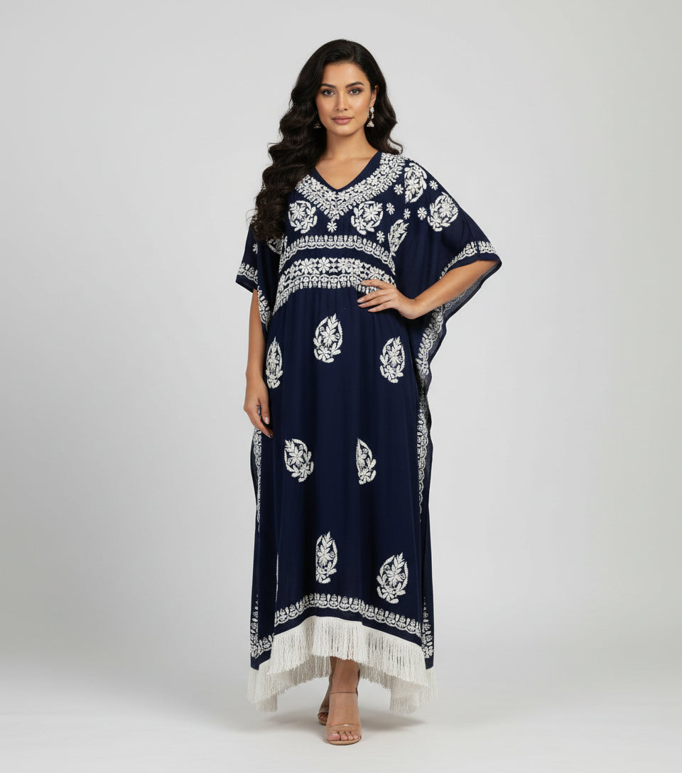 A navy blue Chikankari kaftan dress with intricate white thread embroidery and a V-neckline, standing by a bench with grass and flowers in the background.