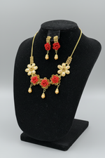 Necklace and earrings set with red flowers and gold accents on a black stand.