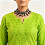 Close-up view of the neckline and chest area of a vibrant lime green cotton short kurti featuring dense, intricate floral embroidery and a keyhole neckline, styled with an ornate silver choker necklace.