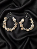Pair of neutral beige seashell hoop earrings with silver-toned beads laid flat on luxurious black satin fabric, handcrafted boho design.
