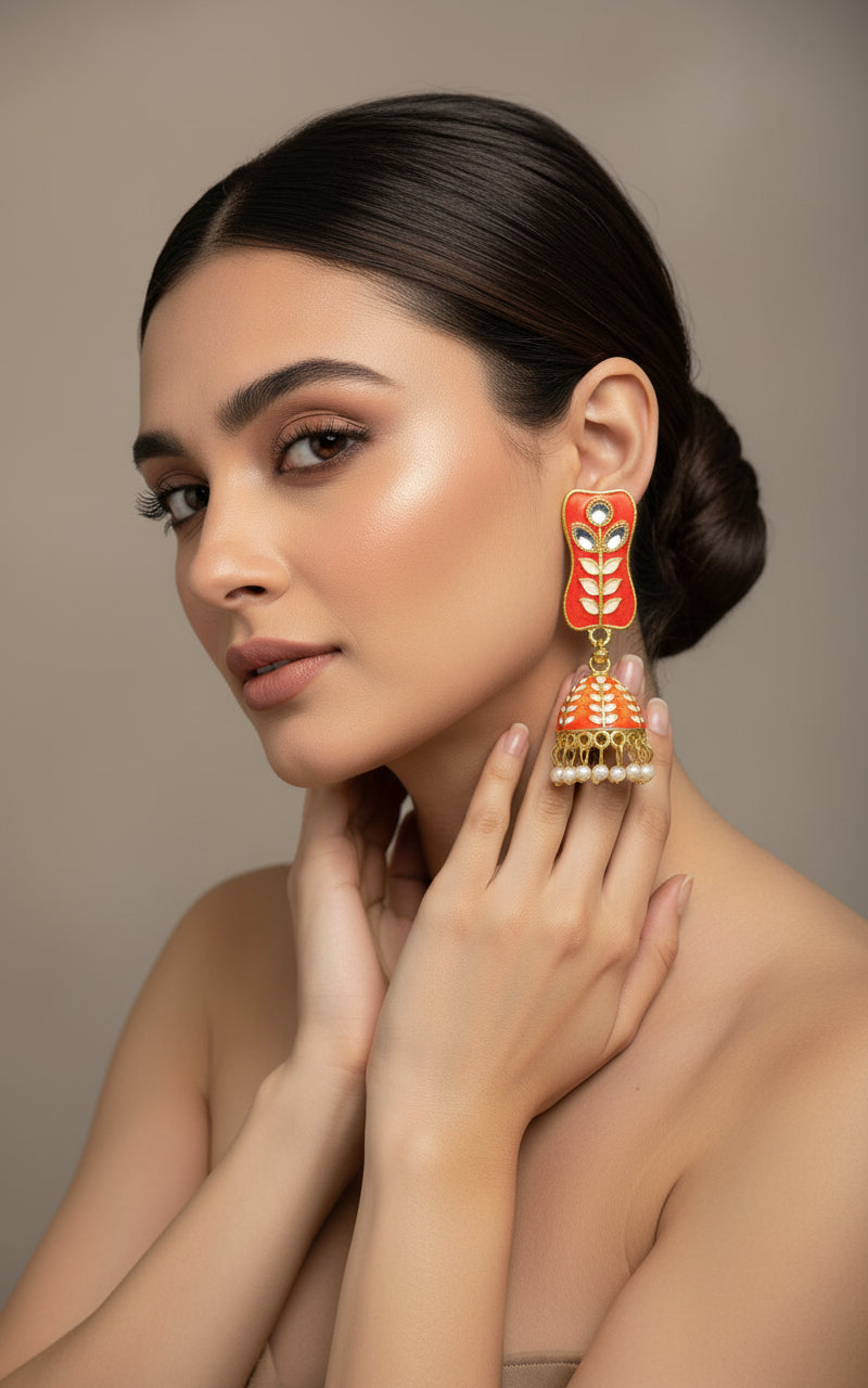 Orange colour pair of gold-platedMeenakari drop Jhumka earrings displayed on a stand, featuring intricate designs and studded with stones.