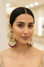 Ornate brass earrings with rose gold polish , red, and pearl details on a model