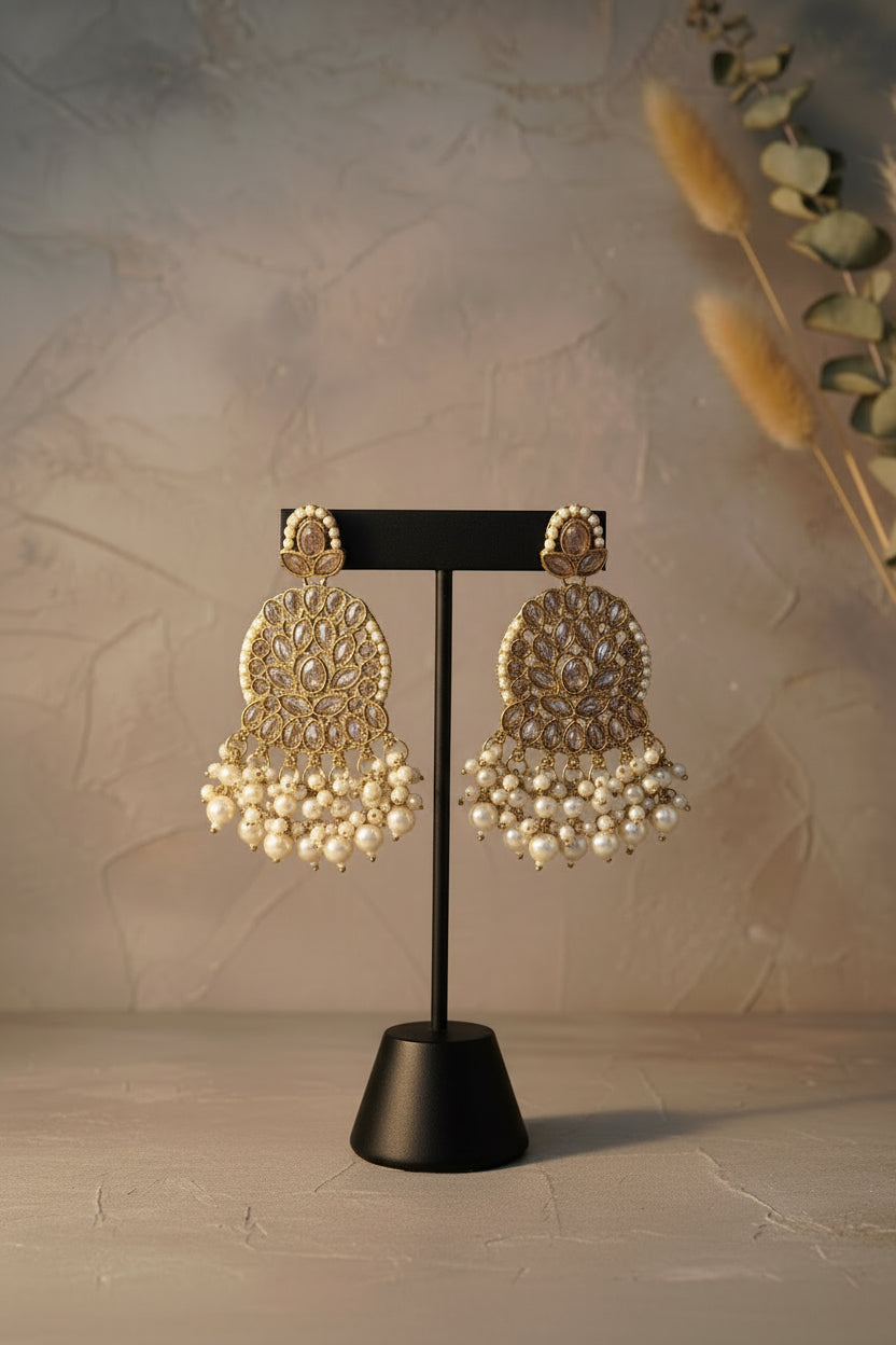 Ornate earrings with gold detailing and pearl beads on a black stand.