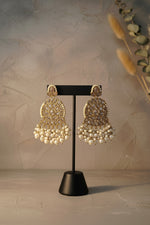 Ornate earrings with gold detailing and pearl beads on a black stand.