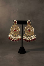 Ornate earrings with pearls and red stones on a black stand.