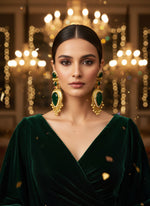 Ornate gold and green gemstone earrings on a textured white surface