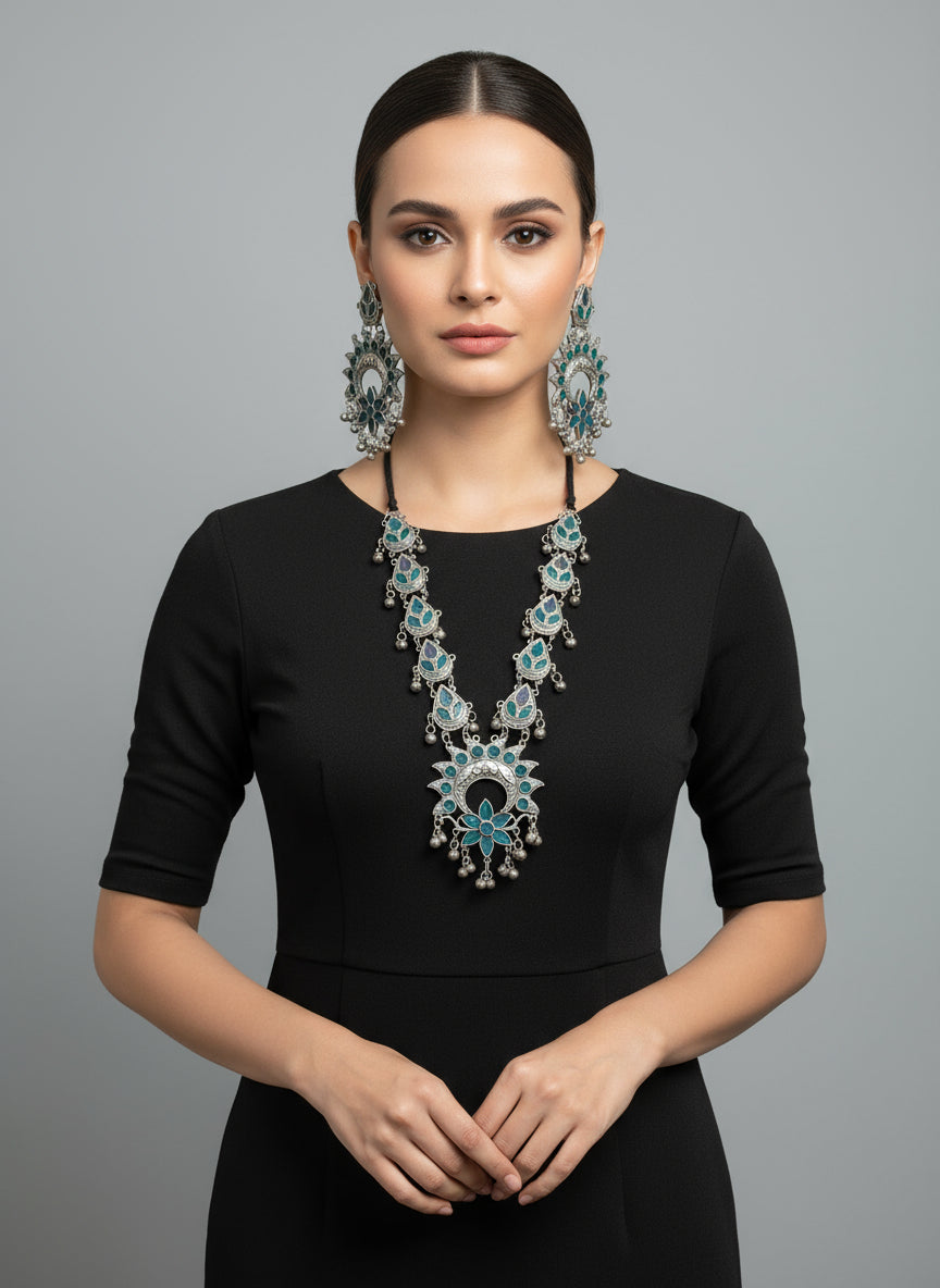 Woman wearing a black outfit with a large turquoise necklace and earrings on a grey background