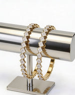 Gold bracelet with diamond accents on a metallic stand against a white background