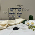 Pair of American diamond earrings with navy blue stone on a stand with measurements indicated.