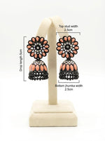 Pair of black brass jhumka earrings displayed on a stand, showcasing a soft peach floral stone stud and matching peach-accented jhumka base.