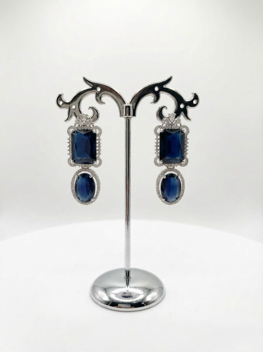 Pair of earrings with blue gemstones on a decorative stand against a white background