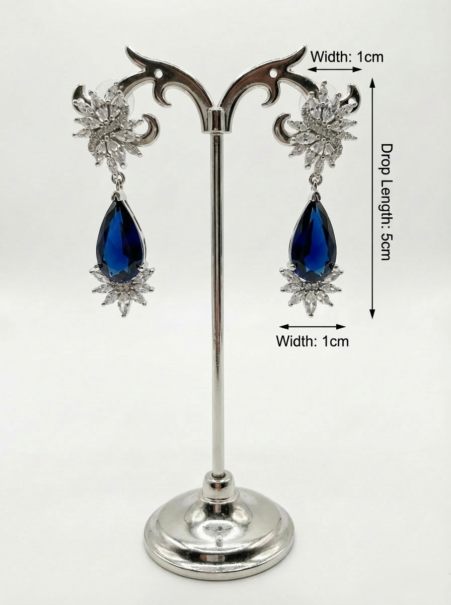 Pair of earrings with blue teardrop-shaped stones on a stand with measurements.