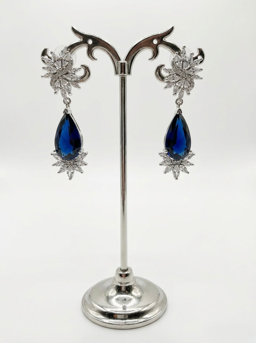 Pair of earrings with blue teardrop stones on a silver stand against a white background