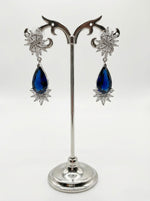 Pair of earrings with blue teardrop stones on a silver stand against a white background