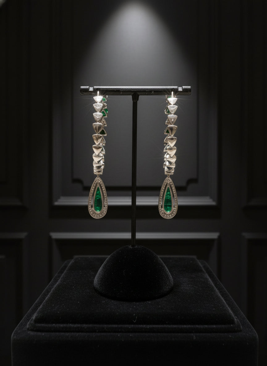 Pair of earrings with green gemstones on a black stand against a dark background