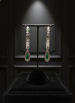 Pair of earrings with green gemstones on a black stand against a dark background