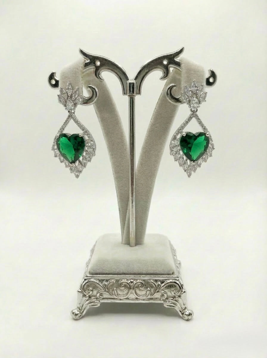 Pair of earrings with green heart-shaped stones on a decorative stand against a white background