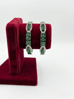 Pair of green gemstone earrings on a red velvet stand against a white background