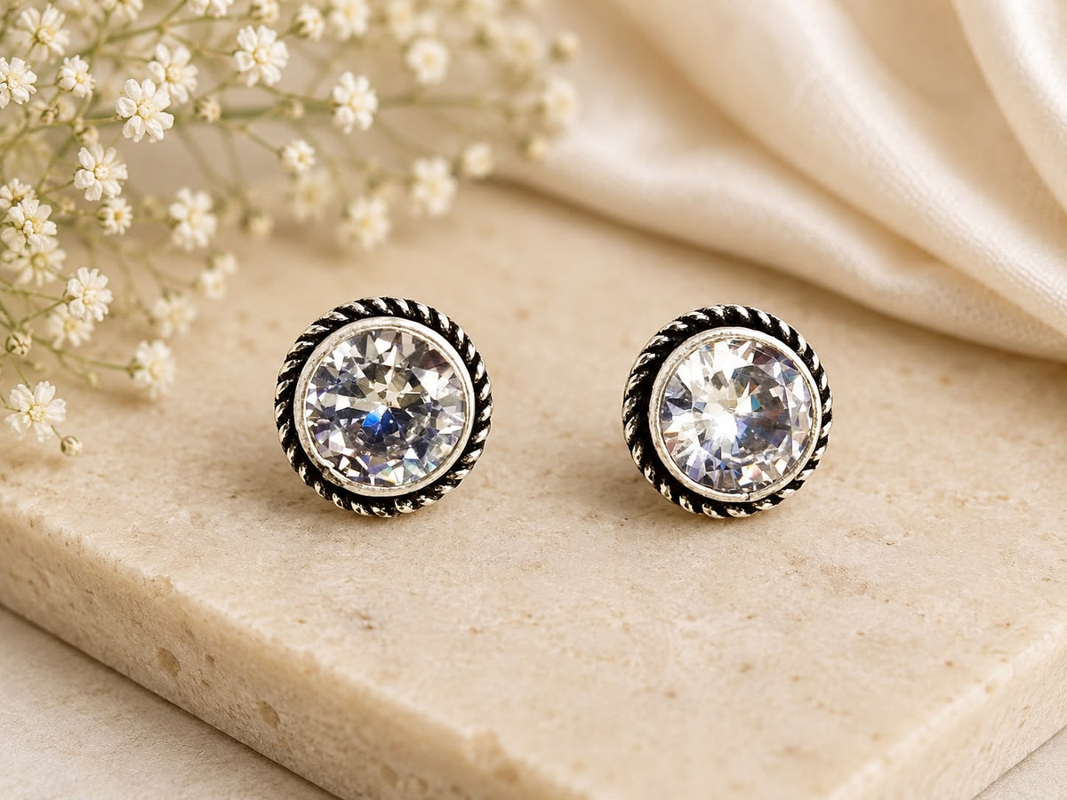 Pair of round stud earrings with clear gemstones on a beige surface with flowers.