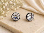 Pair of round stud earrings with clear gemstones on a beige surface with flowers.