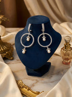Pair of silver brass hoop earrings with central and bottom pearl drops displayed on a professional stand.