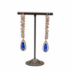 Pair of teardrop-round shaped earrings with blue gemstones on a stand in a jewellery store setting.