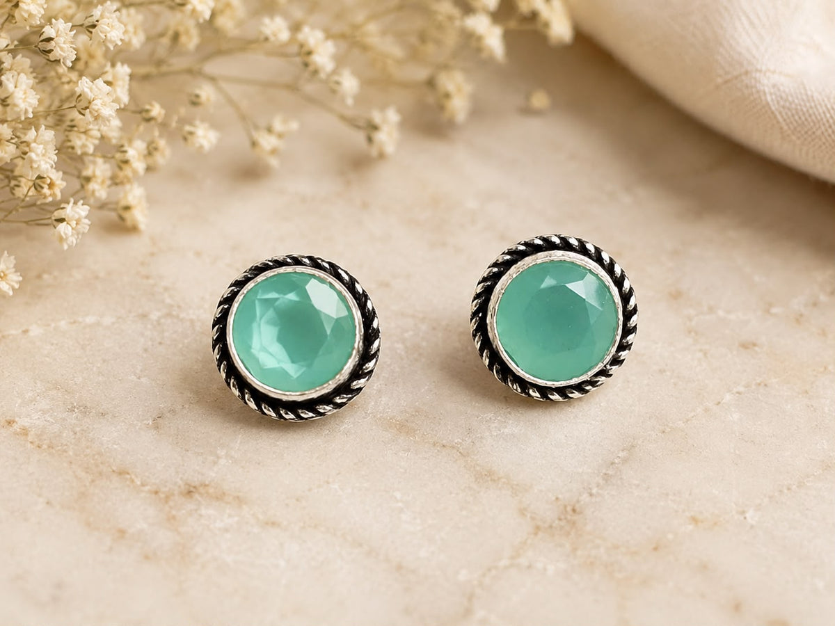Pair of turquoise earrings on a beige marble surface with dried flowers.