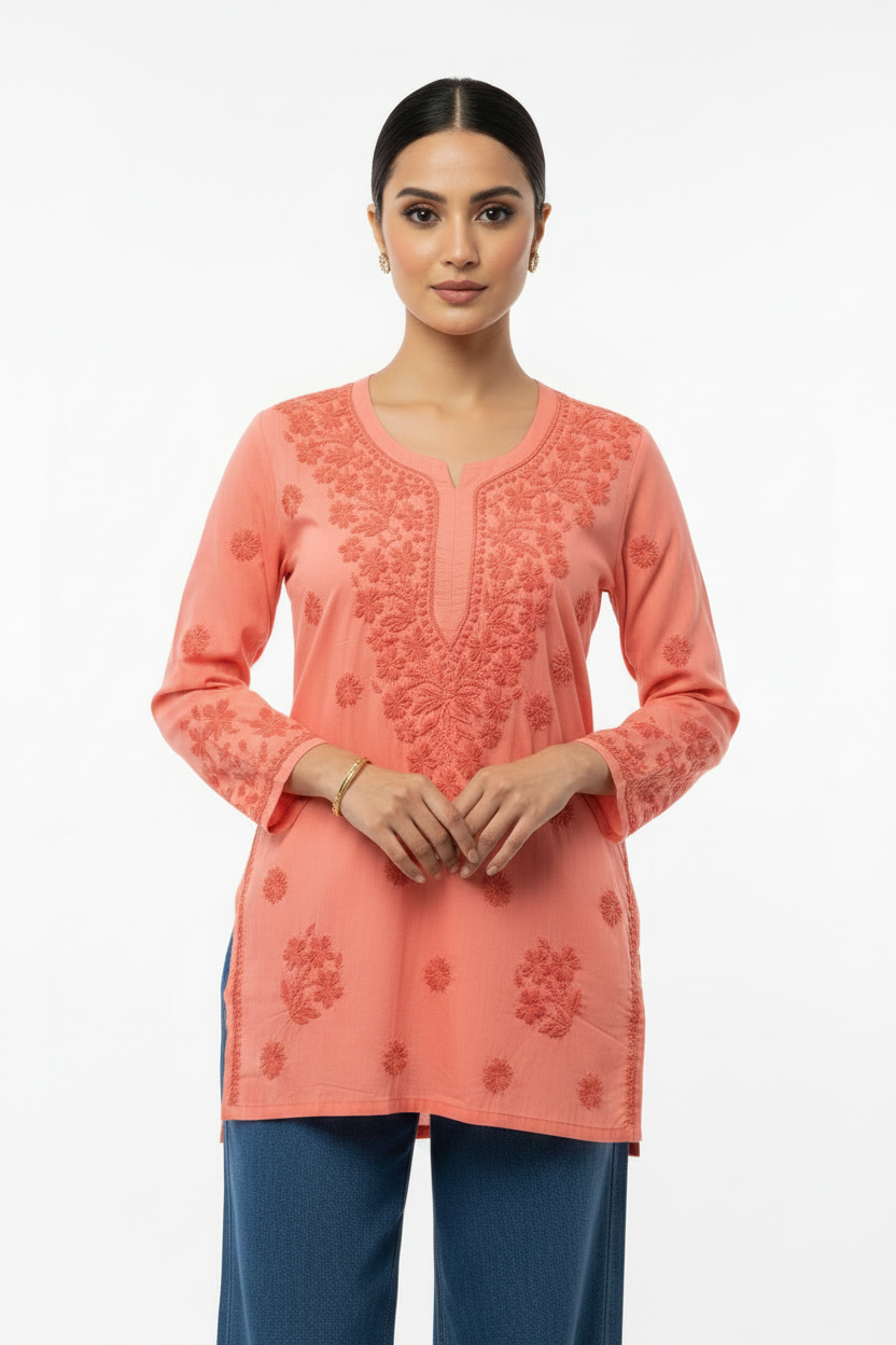 Peach cotton short kurti with intricate chikankari floral embroidery on neckline, yoke and cuffs, displayed on a model against plain white background.