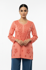 Peach cotton short kurti with intricate chikankari floral embroidery on neckline, yoke and cuffs, displayed on a model against plain white background.