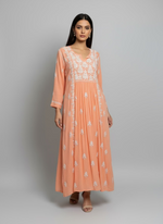 Peach-coloured long dress with white floral embroidery on a rack against a black background