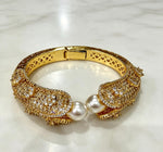 Famaza Couture gold-tone open cuff bracelet featuring two lustrous white pearls meeting at the opening, densely encrusted with sparkling clear pavé crystals, polished gold lattice inner band with hinged clasp, displayed on white marble — luxury bridal statement jewellry.