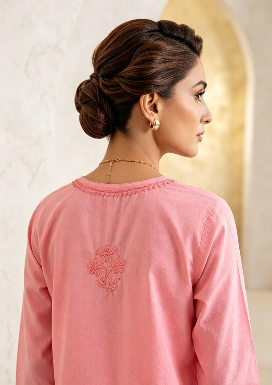 Rear view of a woman wearing a blush pink cotton short kurti featuring a delicate matching pink floral motif embroidered on the back yoke, designed with a square hem line.