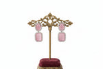 Pink earrings on a decorative gold stand with a blurred background