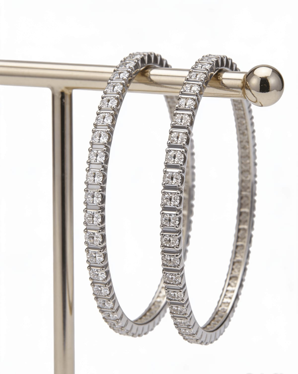 A pair of high-quality silver-toned American diamond bangles with a continuous single row of stones in a modern square-prong setting, displayed on a gold-finished jewelry stand.