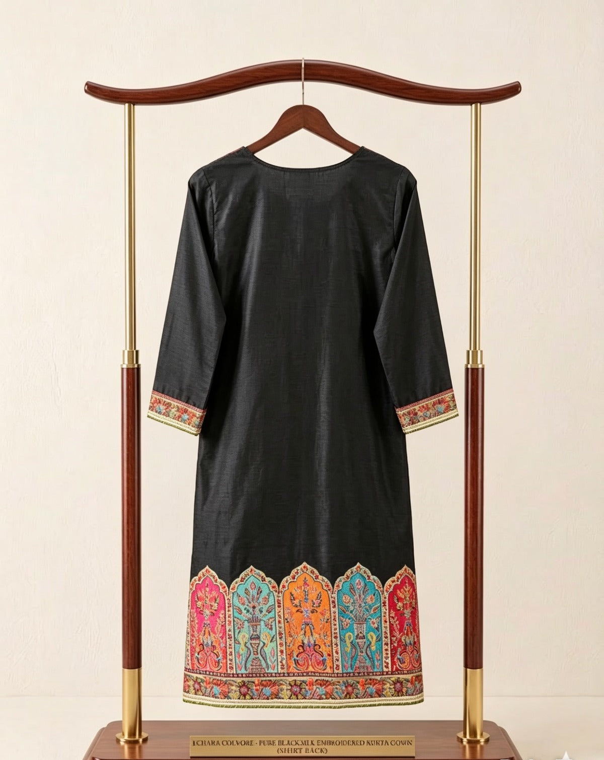 Back view of premium black silk kurta featuring intricate Kanni embroidery, detailed Zari work on borders, displayed on an elegant wooden and gold stand against a clean white background; showcasing rich multicolored traditional motifs and fine craftsmanship.